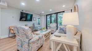 Un salon moderne avec un canapé, des fauteuils, une table basse et un téléviseur fixé au mur.