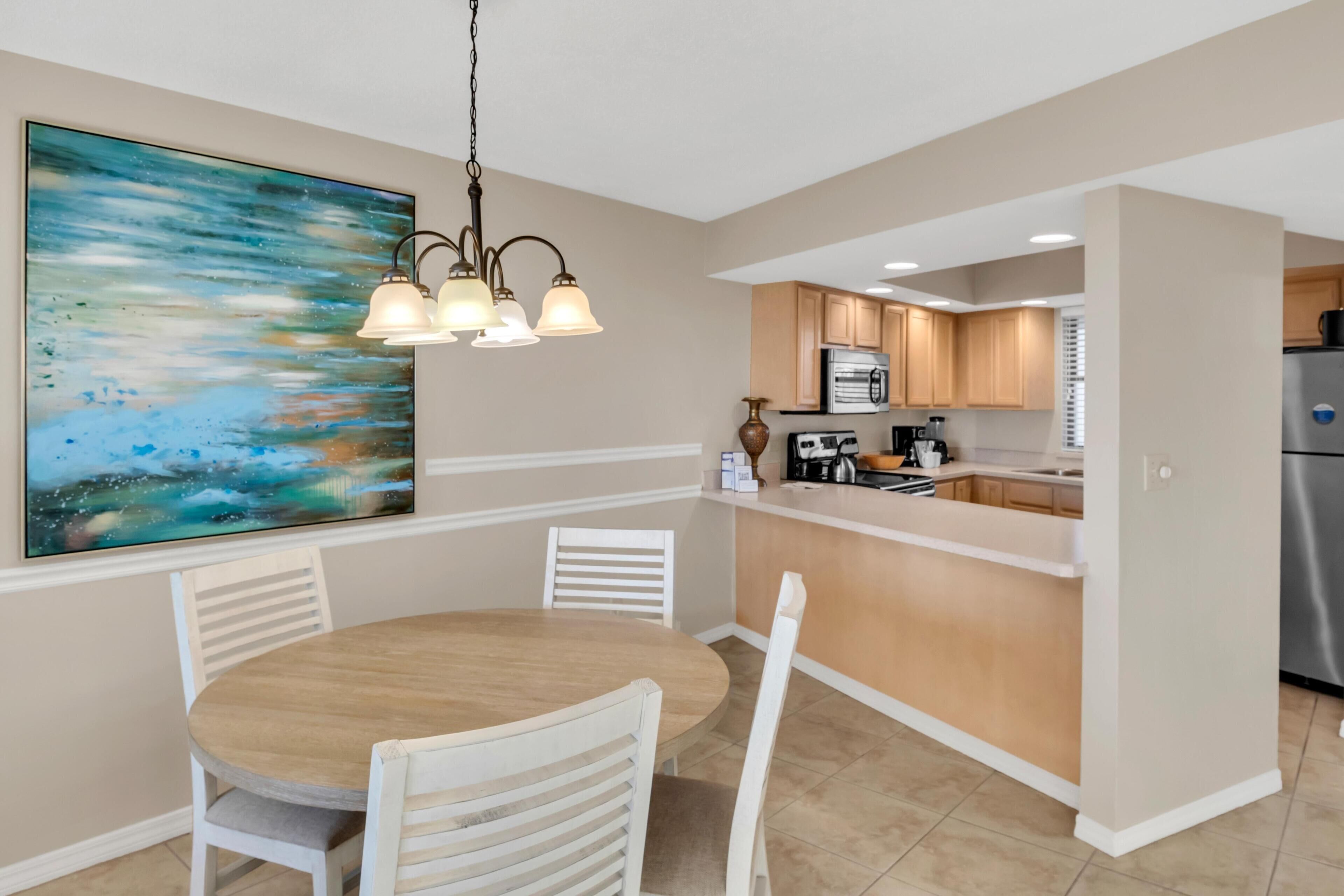 A modern kitchen with white cabinets, a central island, and a dining area with a round table and chairs.