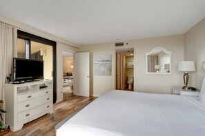 Ein Hotelzimmer mit einem großen Bett, einem Fernseher auf einem Schminktisch, einem Badezimmer mit Spiegel und einer Tür, die in einen weiteren Raum führt.