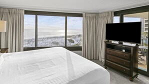 A hotel room with a large bed, a flat-screen TV, a dresser, and a balcony with a view of a snowy landscape. - Modern 4th-Floor Condo w/ Gulf Views & Golf Cart! (Miramar Beach)
