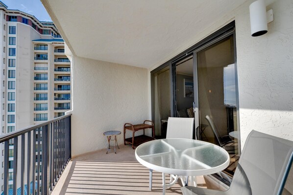 A balcony with a glass door, a small round table, and two white chairs.