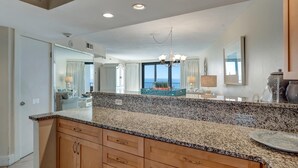 Eine Küche mit Granit-Arbeitsplatten, Holzschränken und einer zentralen Kochinsel. Über der Insel hängt eine Chandelier, und ein großes Fenster bietet einen Blick ins Freie.