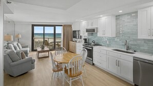 Una cocina moderna con armarios blancos, una mesa de comedor de madera y vista al océano.