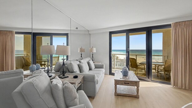Una sala de estar moderna con un sofá grande, una mesa de centro y vistas a la playa a través de amplios ventanales.