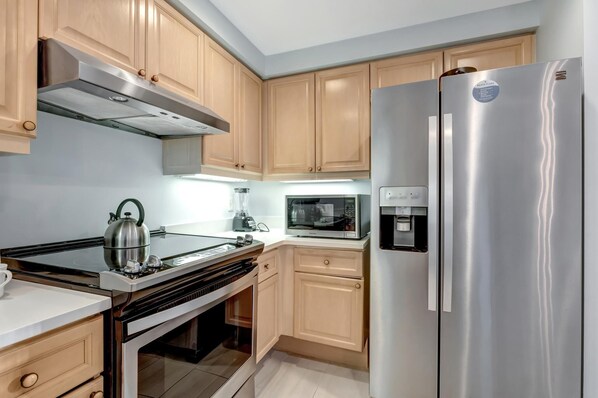 Una cocina moderna con armarios de madera, electrodomésticos de acero inoxidable, una estufa a gas, un microondas y un refrigerador.