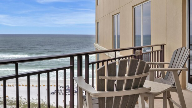 Een balkon met twee Adirondack stoelen, uitzicht op de oceaan en een gebouw met grote ramen.