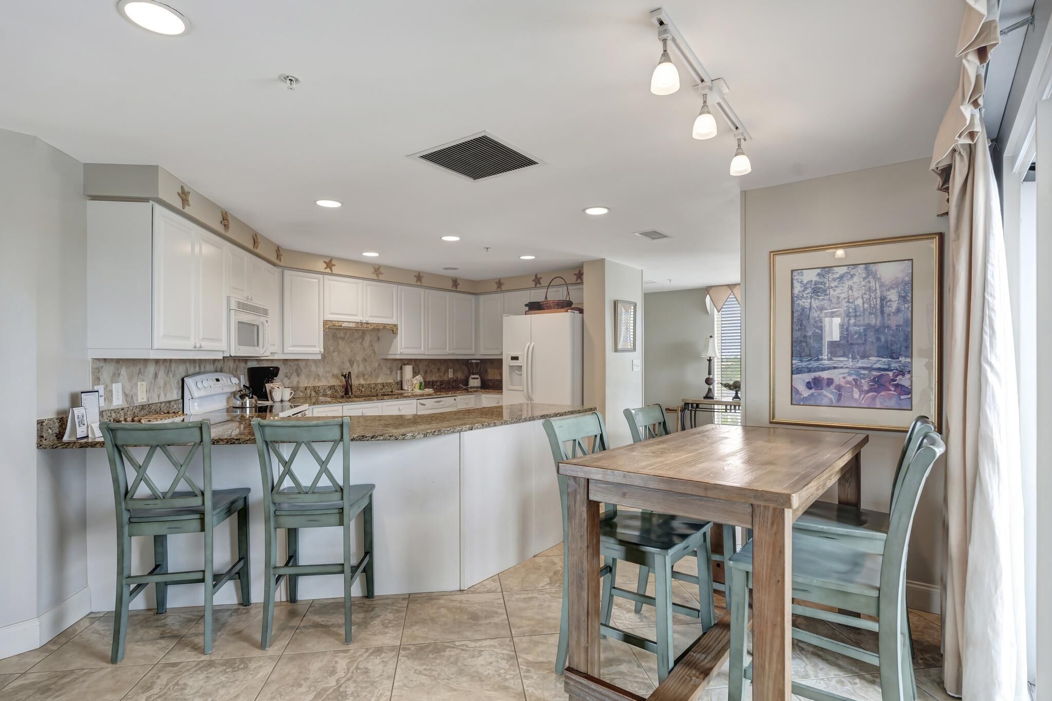 A modern kitchen with white cabinets, a granite countertop, and a dining area with a wooden table and chairs.