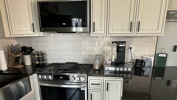 A modern kitchen with stainless steel appliances, white cabinetry, and a black countertop.