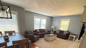 A spacious living room with a wooden dining table, two sofas, a coffee table, and a TV.