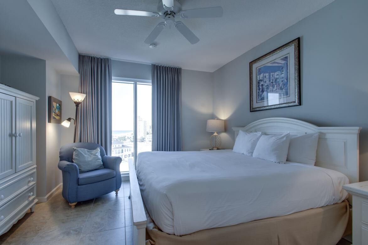 Habitación de hotel con una cama grande, una silla, ventilador de techo y vistas a la ciudad desde la ventana.