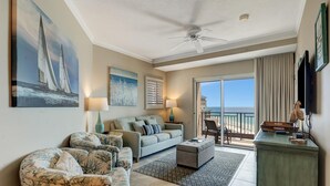 Un salon comprenant un canapé, des fauteuils, une table basse et un téléviseur. Il y a également un balcon avec vue sur l’océan.