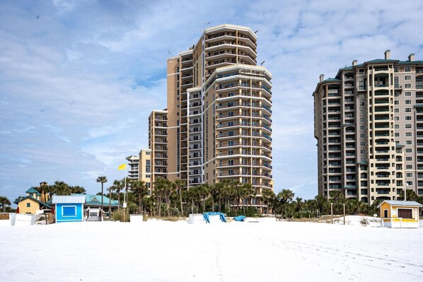 A high-rise hotel with multiple balconies, a beach view, and a small beachside structure.