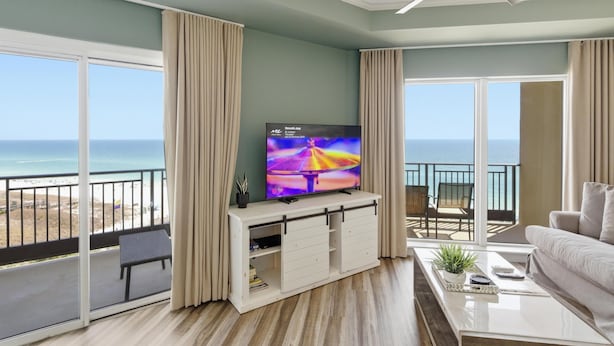 Una sala de estar con televisor, un balcón con vista al océano y un ventilador de techo.