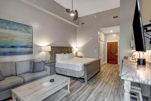 Ein modernes Hotelzimmer mit Bett, Sofa, Couchtisch, einem Gemälde und einer Küchenzeile.