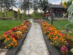 Un sentier bordé de parterres de fleurs aux couleurs vives, qui mène à un chalet doté d’une façade en pierre et de détails en bois.