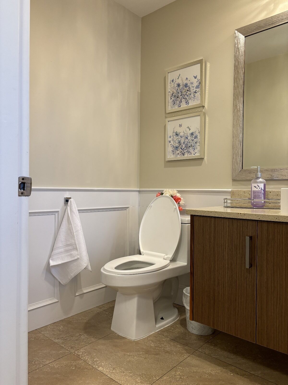 A bathroom with a toilet, a sink, a mirror, and two framed floral pictures on the wall.