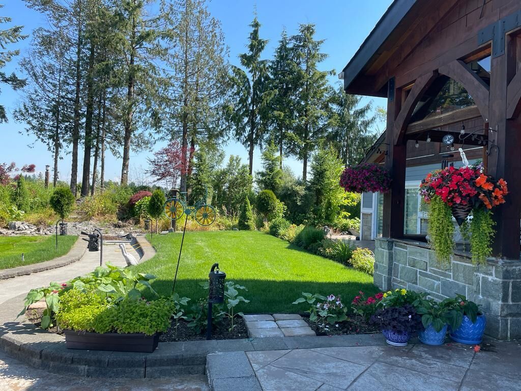 En välskött trädgård med en stenlagd gång som leder fram till ett hus med en träfasad och hängande blomkorgar.