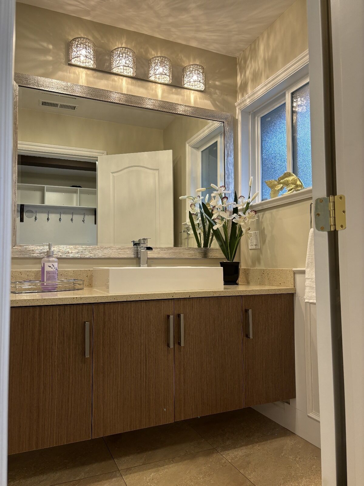 Een moderne badkamer met een grote spiegel, drie hangende lampen, een wastafel en houten kastjes.