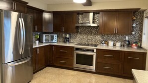 A modern kitchen with dark wooden cabinets, stainless steel appliances, a tiled backsplash, and a granite countertop. - Mountain View Farm Experience! (Pitt Meadows)