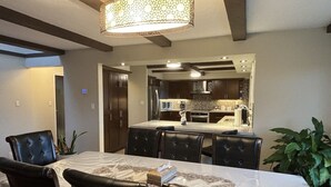 A dining area with a table and chairs, a kitchen in the background, and a hanging light fixture. - Mountain View Farm Experience! (Pitt Meadows)