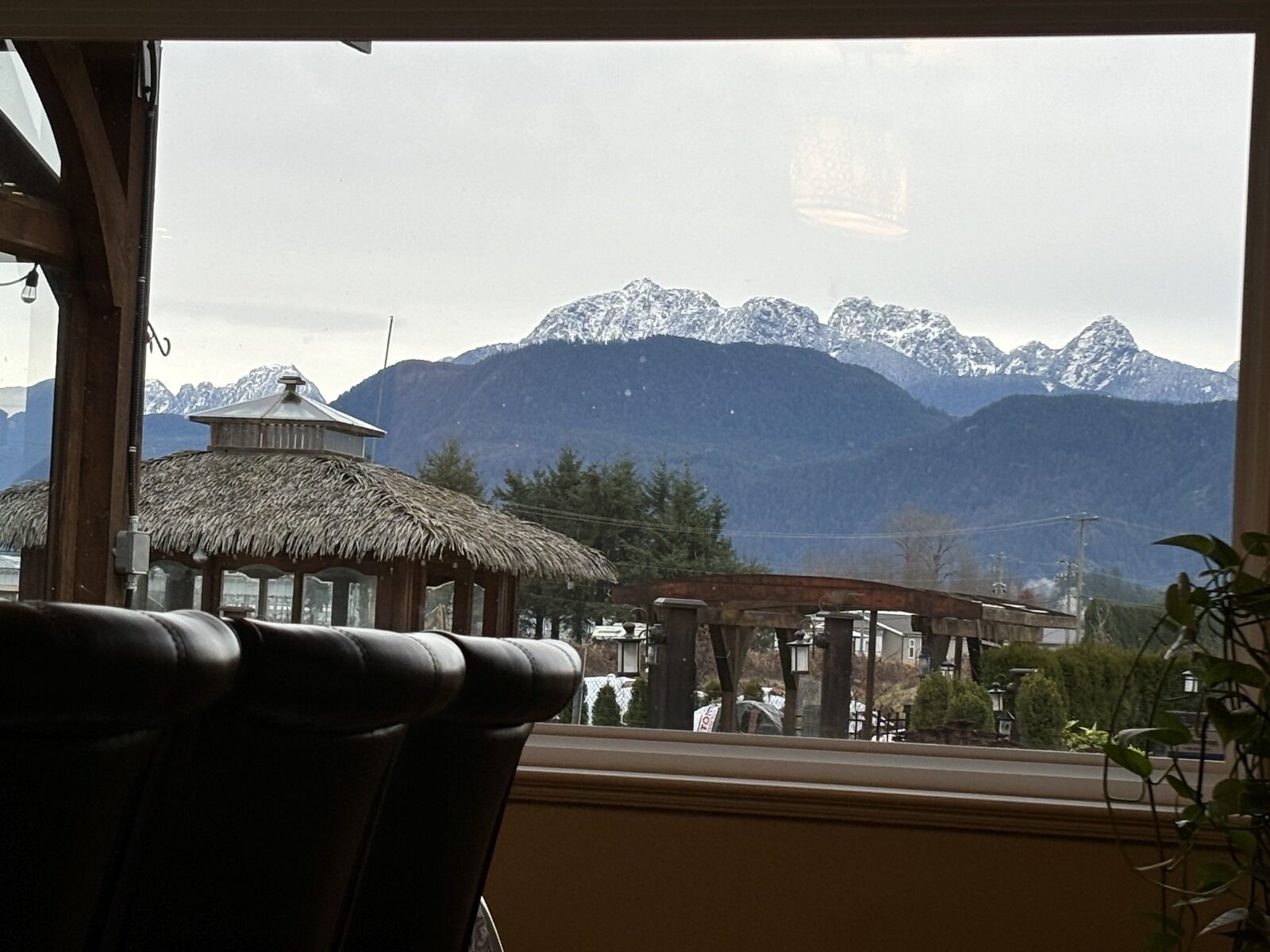 A view from a window overlooking a mountain range with a thatched-roof structure and a gazebo in the foreground.