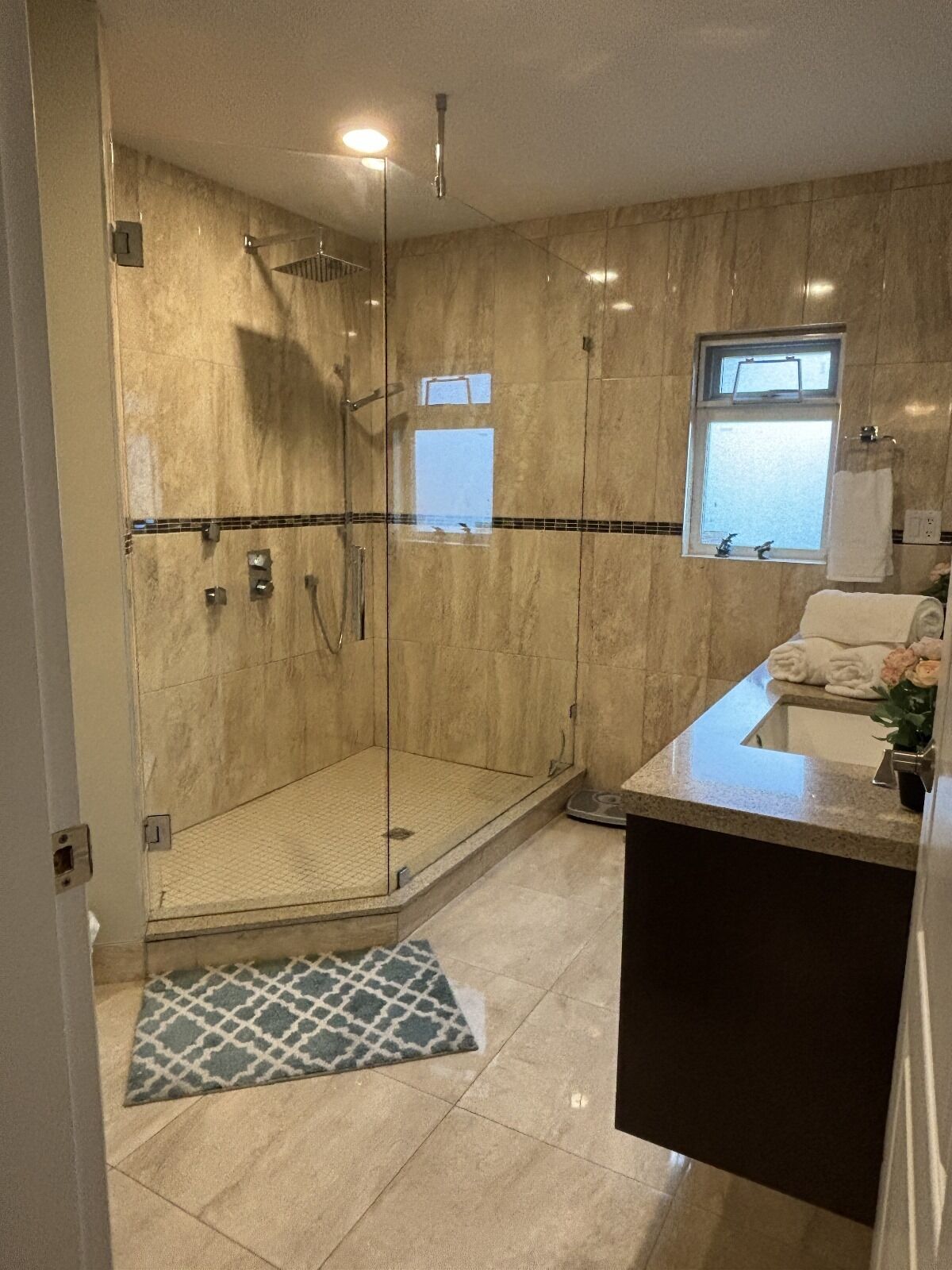 A modern bathroom with a glass-enclosed shower, a sink with a countertop, and a window providing natural light.