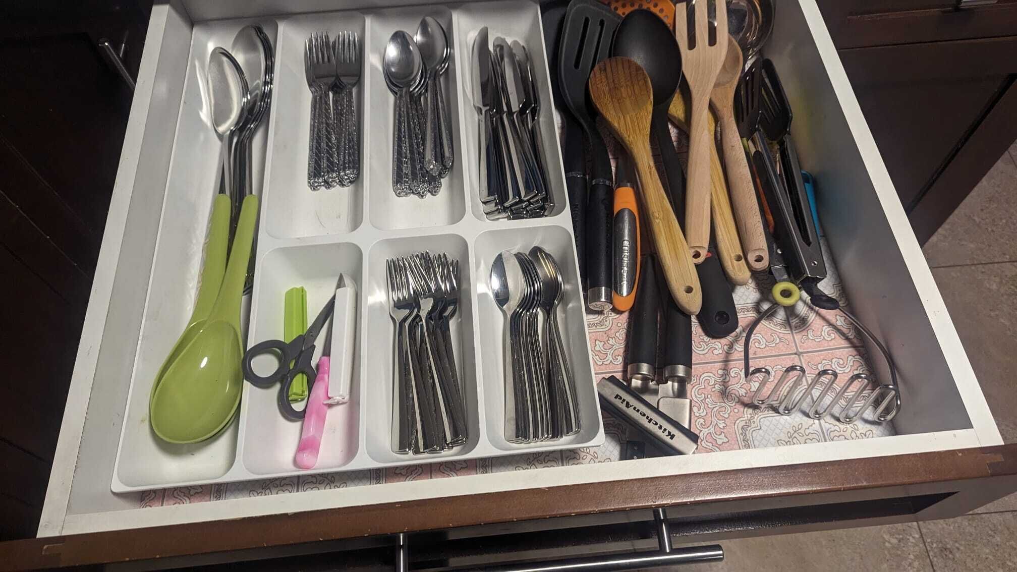 A drawer with various kitchen utensils and tools, including spoons, forks, knives, scissors, and a pair of tongs.
