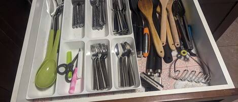 A drawer with various kitchen utensils and tools, including spoons, forks, knives, scissors, and a pair of tongs.