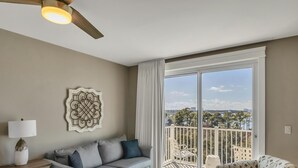 Un salon avec un canapé gris, une table basse ronde et un balcon avec des chaises blanches.