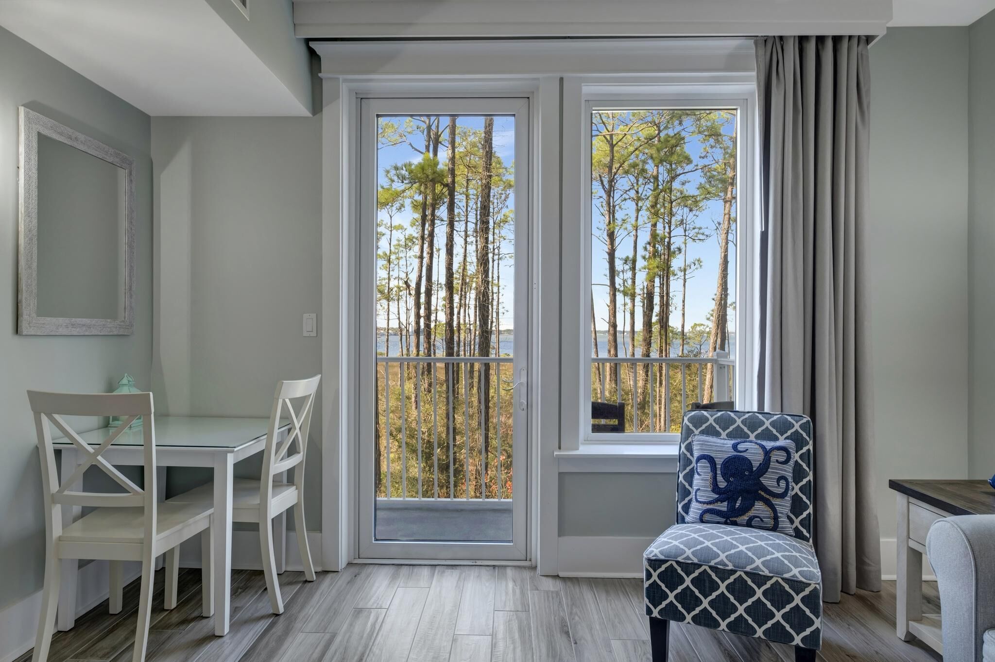 Una stanza con una porta vetrata che dà su un balcone, un tavolo con sedie e una poltrona con motivo decorativo.