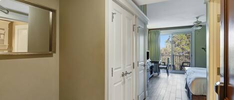 Una habitación de hotel con cama, un banco, un escritorio y un balcón con vistas a árboles.