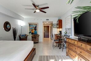 Habitación de hotel con cama, escritorio, silla, televisor y ventilador de techo.