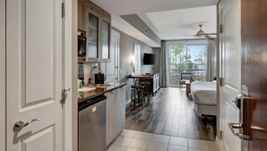 Ein modernes Hotelzimmer mit Küchenzeile, einem Esstisch und einem großen Fenster mit Blick auf Bäume.