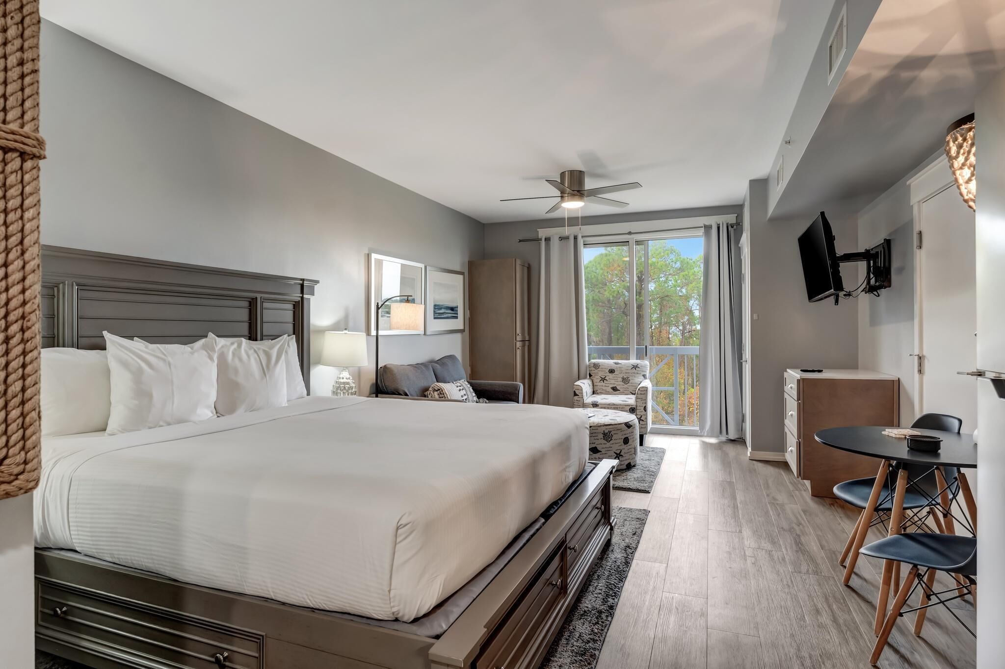Une chambre d’hôtel moderne dotée d’un grand lit, d’un bureau avec des chaises, d’un ventilateur de plafond et offrant une vue sur l’extérieur.