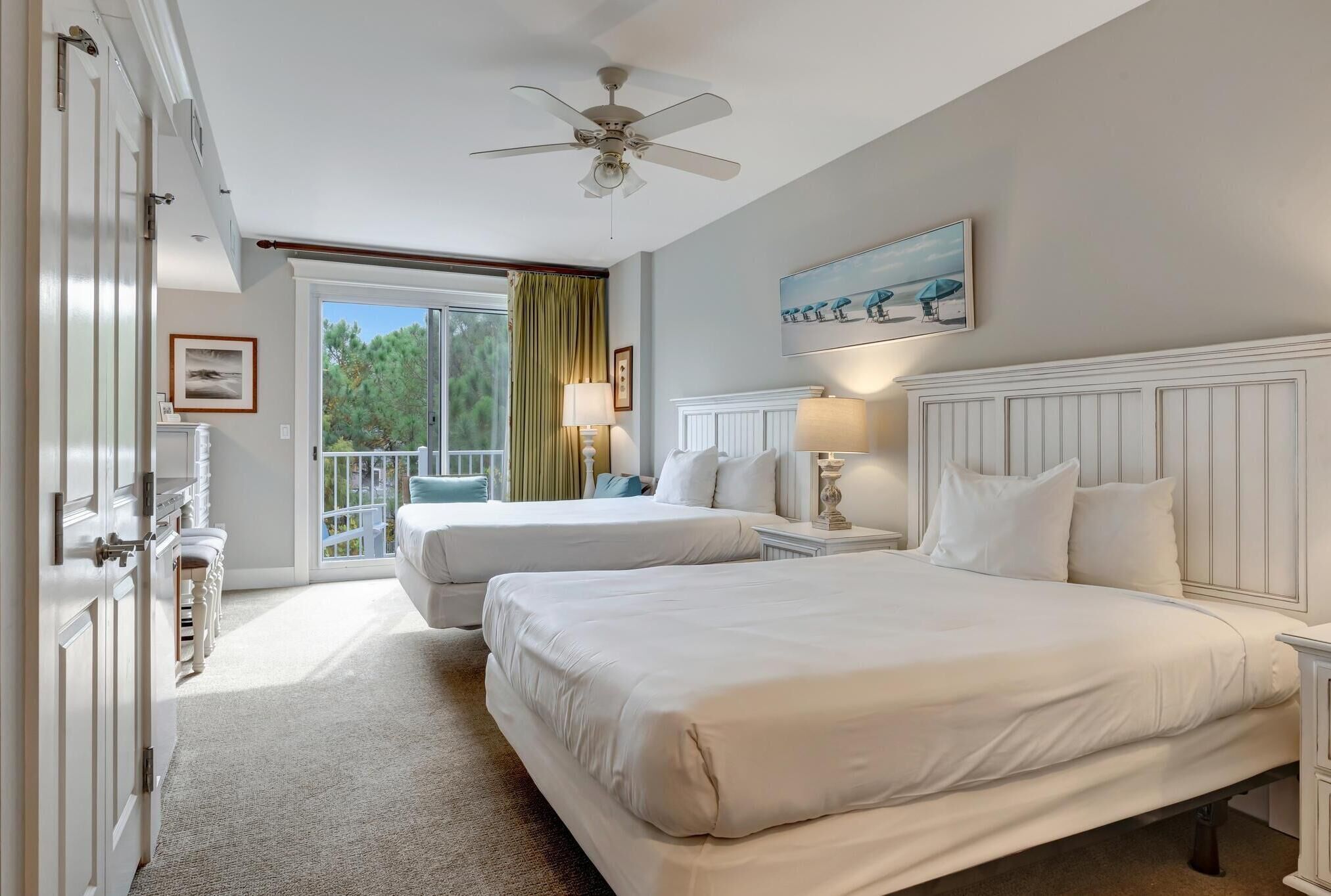 A hotel room with two beds, a ceiling fan, a window with curtains, and a painting on the wall.
