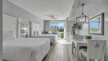 Habitación de hotel con dos camas, un escritorio, una silla, ventilador de techo y balcón con vistas.