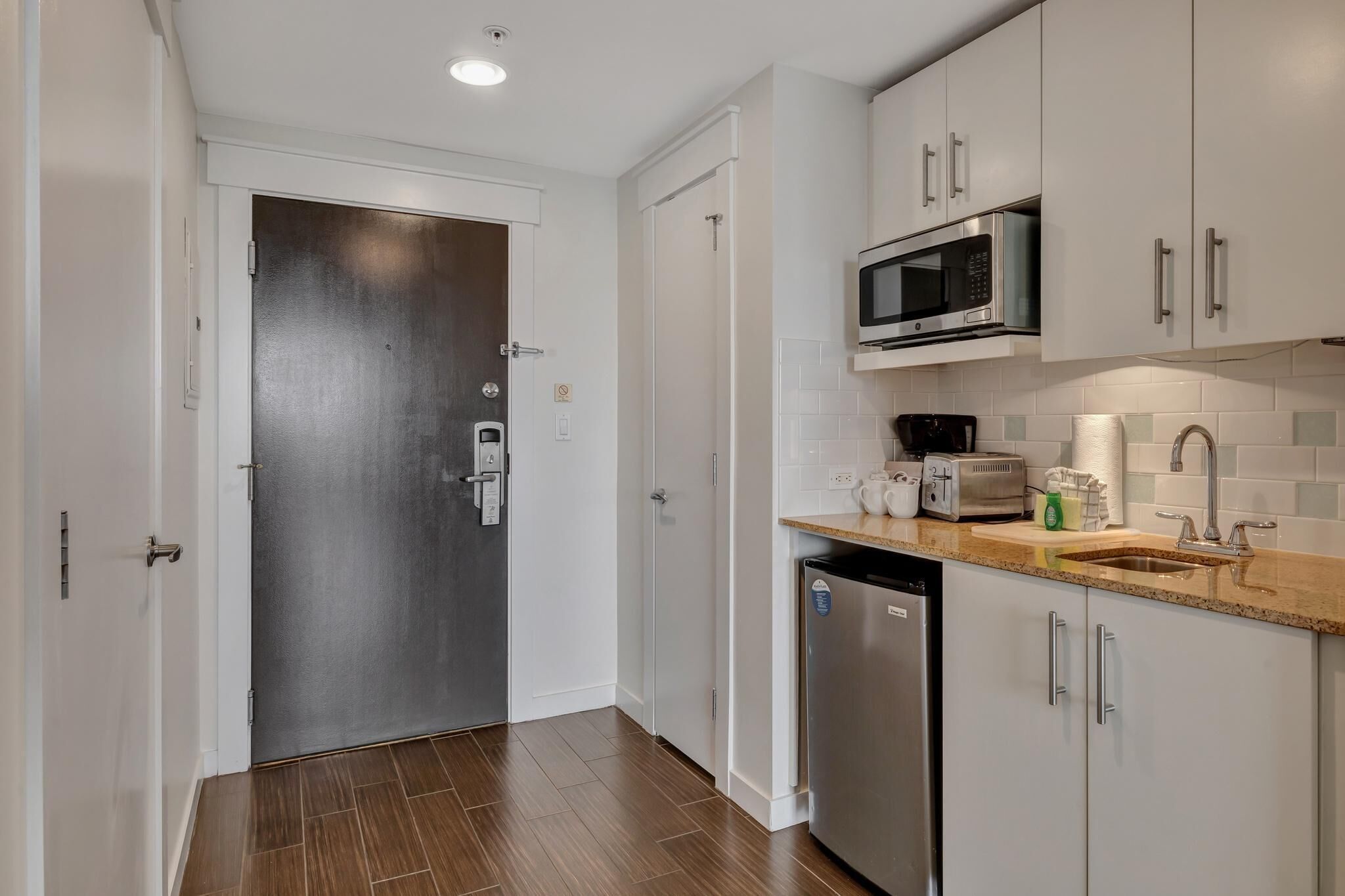 A modern kitchen with white cabinets, a stainless steel dishwasher, a microwave, and a coffee maker.