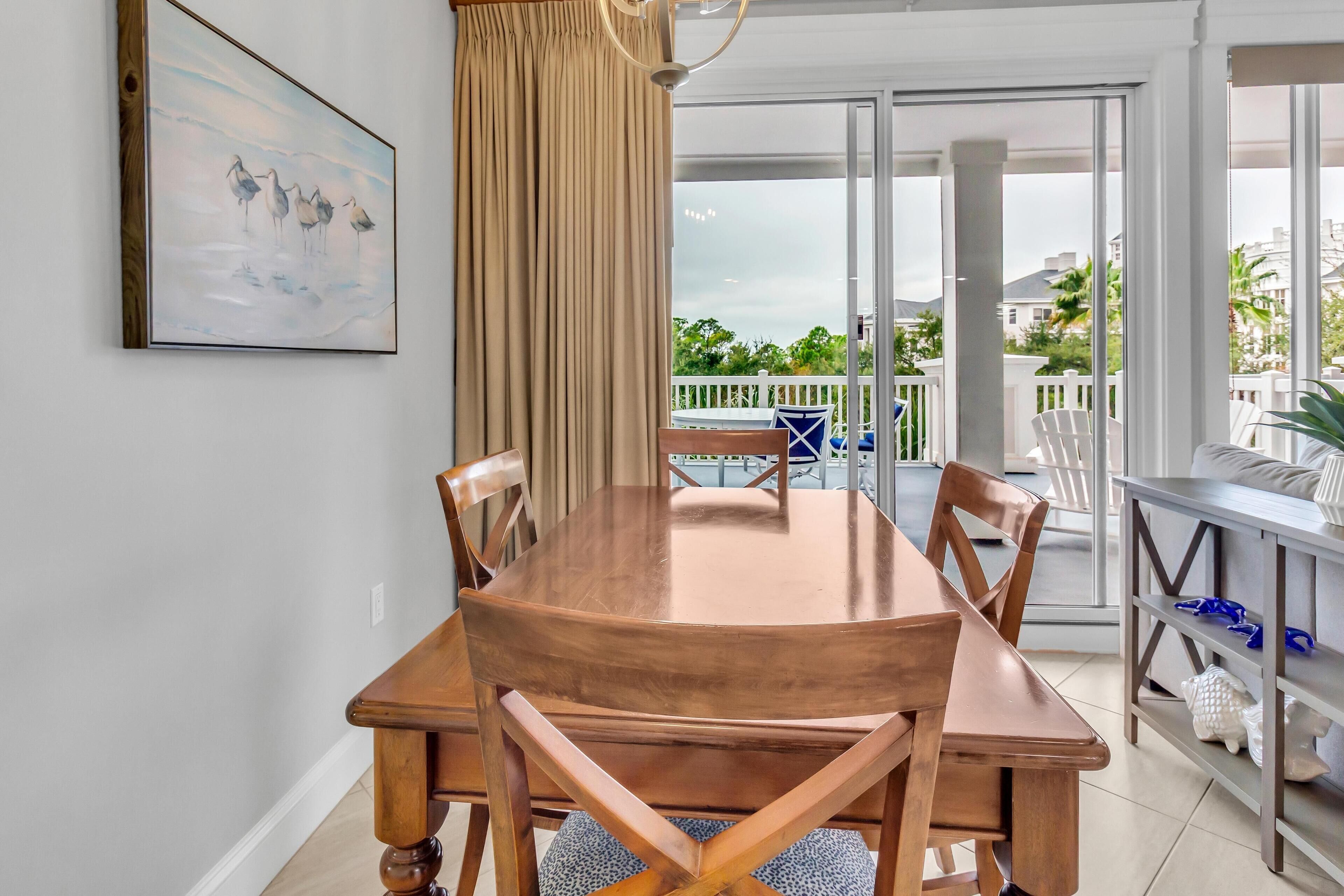 Un comedor con una mesa y sillas de madera, un cuadro en la pared y vistas al exterior a través de un ventanal corredero.