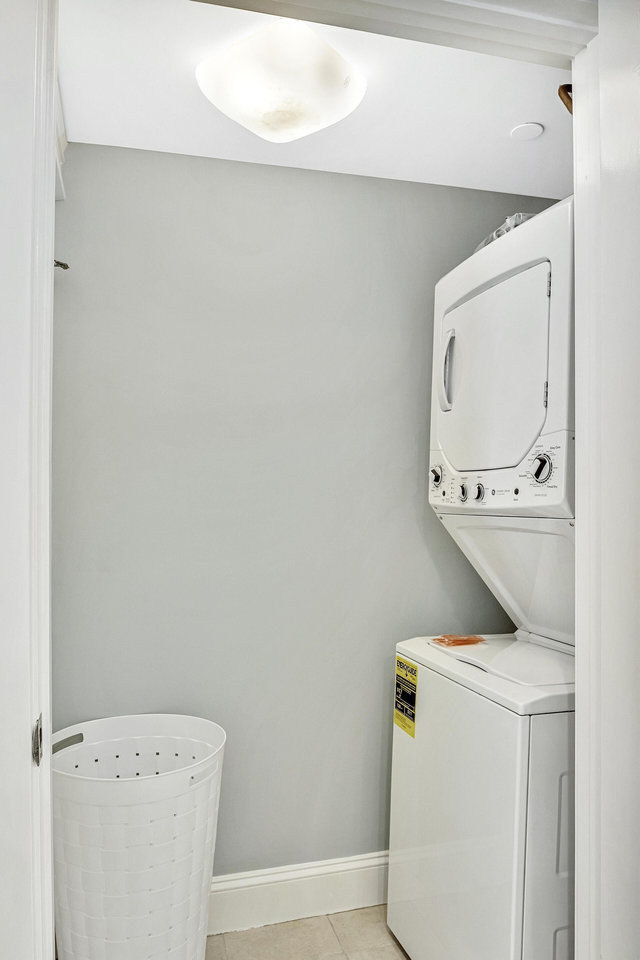 A laundry room with a stacked washer and dryer, a white laundry basket, and a light switch on the wall.