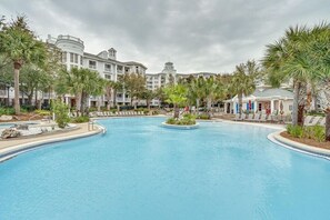 A large, curved swimming pool with lounge chairs and palm trees, surrounded by multi-story buildings with balconies. - Serene Choctawhatchee Bay Views from 4th Floor One Bedroom, Two Bathroom Condo with Large Private Balcony at Sandestin Golf and Beach Resort! (Miramar Beach)