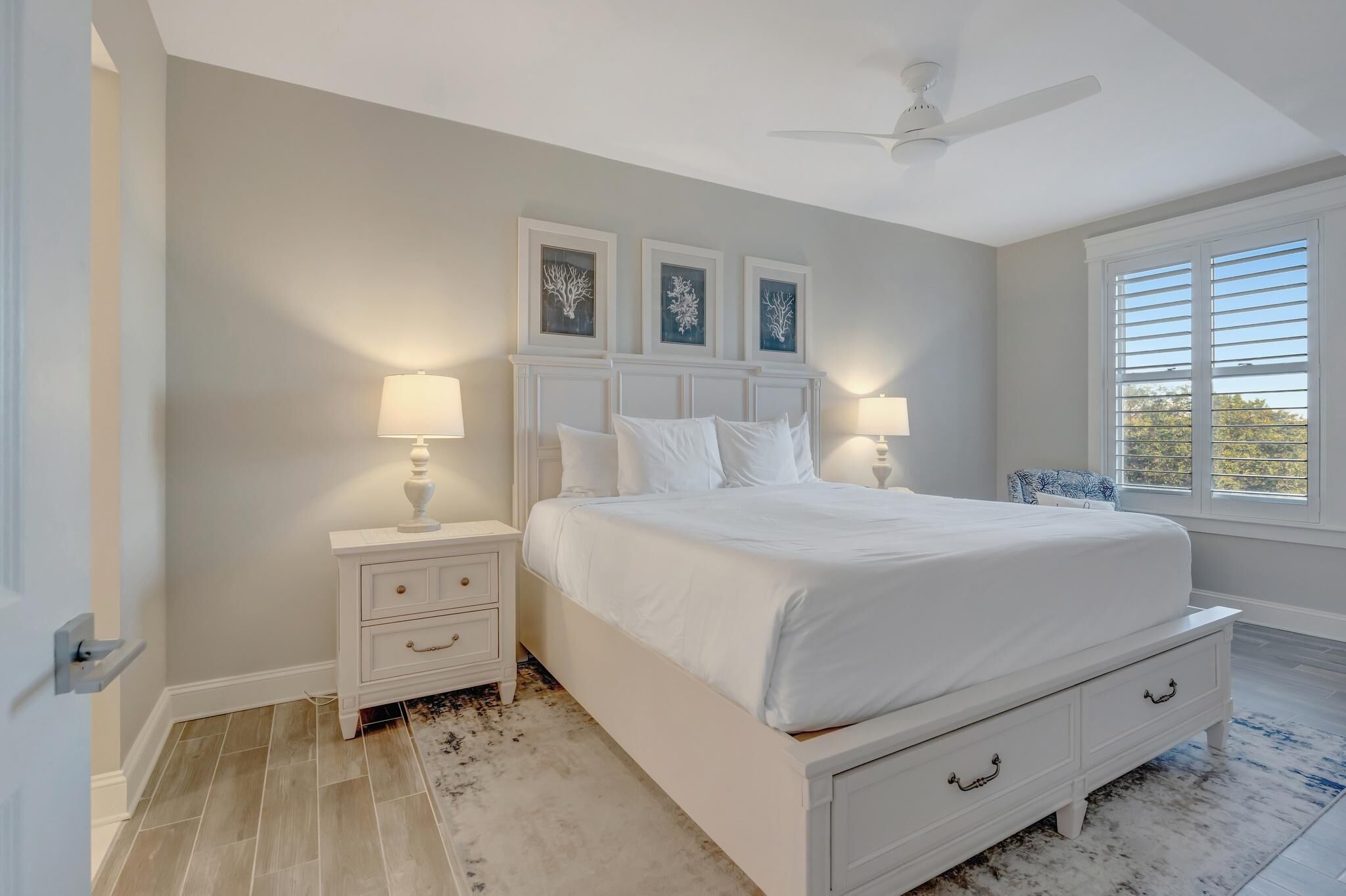 A bedroom with a bed, nightstands, a ceiling fan, and framed artwork on the wall.