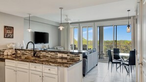 A modern kitchen with a large island, a dining area with a view, and a balcony with outdoor seating. - Serenity in Coastal Elegance: 1-Bedroom, 2-Bath Retreat at Sandestin Golf and Beach Resort! (Miramar Beach)