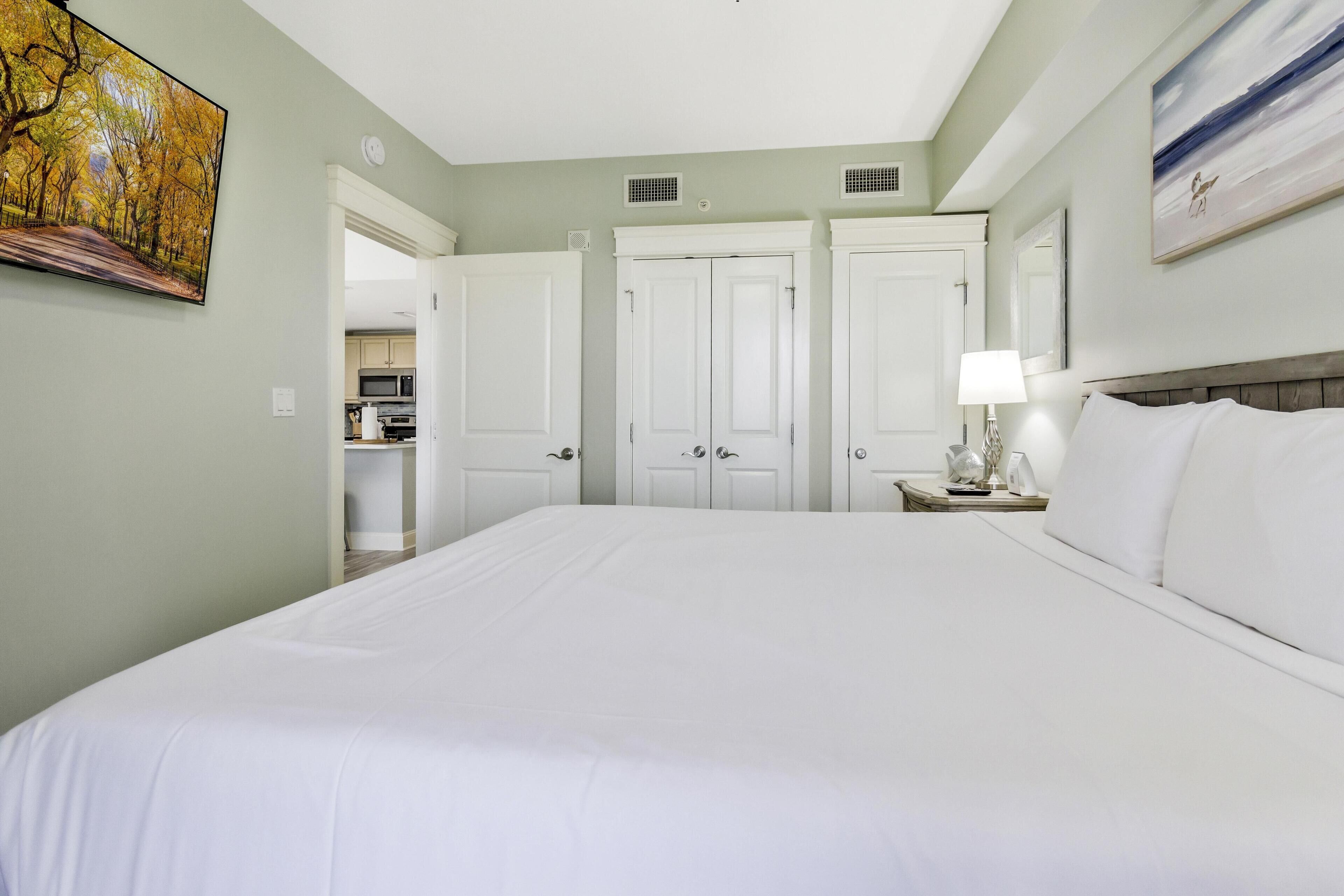 A hotel room with a large bed, a nightstand with a lamp, and a painting on the wall.