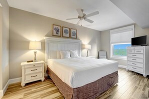 Ein Schlafzimmer mit einem großen Bett, einem Deckenventilator, einem Nachttisch mit Lampe, einer Kommode und einem Fenster mit Blick.