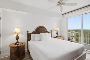 Habitación de hotel con una cama grande, dos lámparas de noche, ventilador de techo y balcón con vistas.