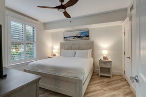 Ein Schlafzimmer mit einem Bett, einem Deckenventilator, einem Nachttisch mit Lampe und einem Bild an der Wand.