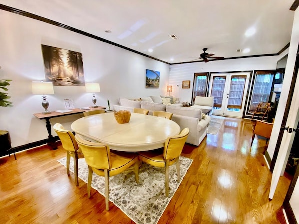 A modern living room with a round dining table, yellow chairs, a sofa, and a ceiling fan.