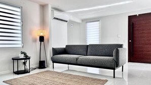 A modern living room with a grey sofa, a standing lamp, and a small table with a plant. - Five-Minute Elegance: New Spacious Home with Pool (Carolina)
