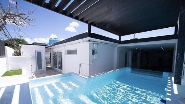 A modern outdoor swimming pool with a covered area, clear blue water, and a view of the sky. - Five-Minute Elegance: New Spacious Home with Pool (Carolina)