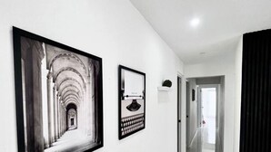 A hallway with white walls, a framed photograph of a corridor, and a framed picture of a person. - Five-Minute Elegance: New Spacious Home with Pool (Carolina)